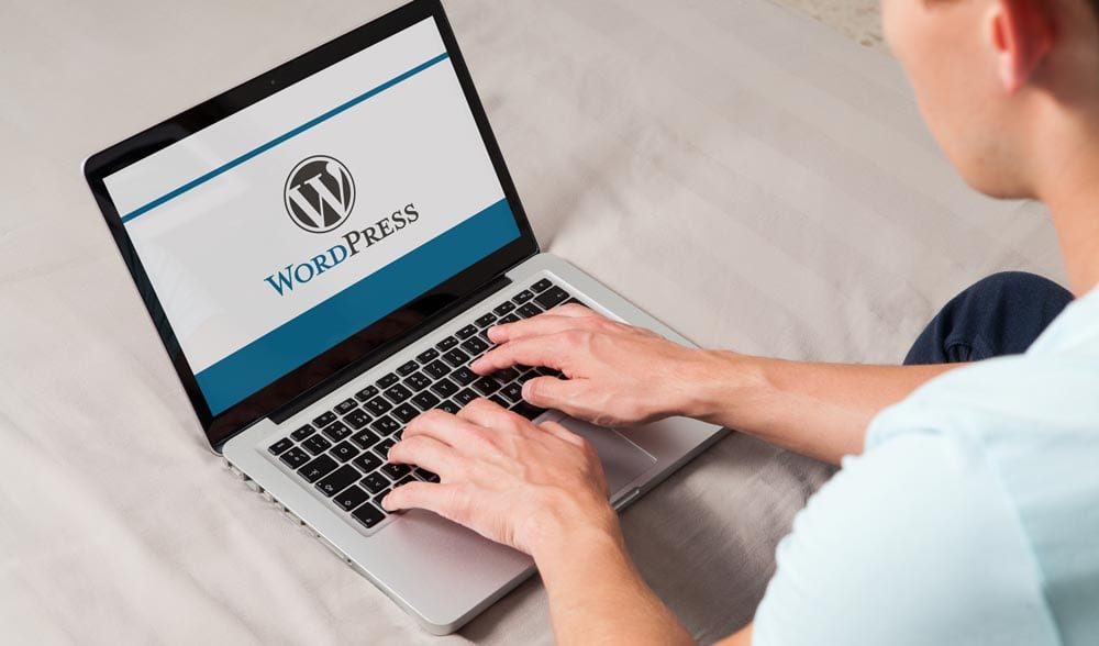A man using a laptop displaying the WordPress logo