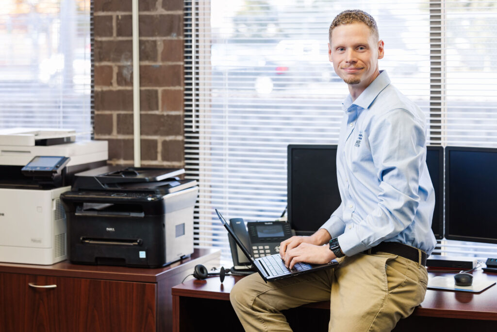 Saltech employee leaning against a desk, and typing on a laptop