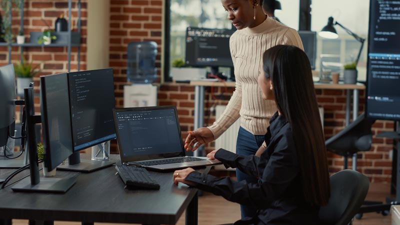 Two woman looking at code on a laptop together