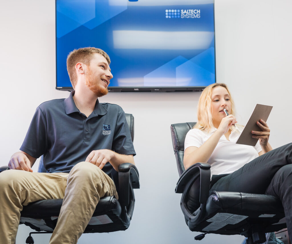 Two Saltech employees sitting in office chairs discussing notes