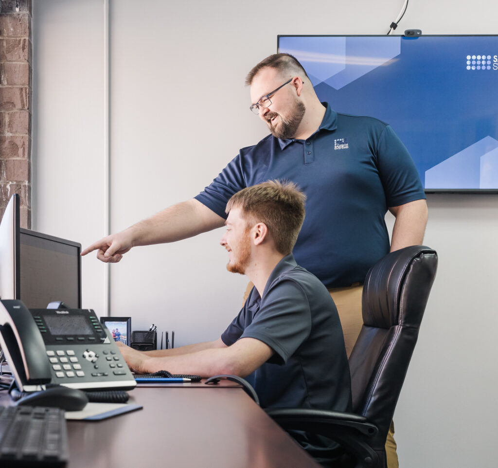 A Saltech employee helping his coworker at his computer