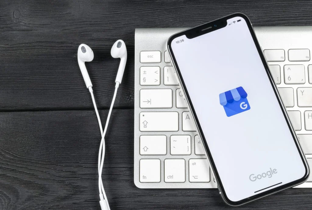 A phone with Google Shop on the screen on top of a keyboard that's next to white headphones